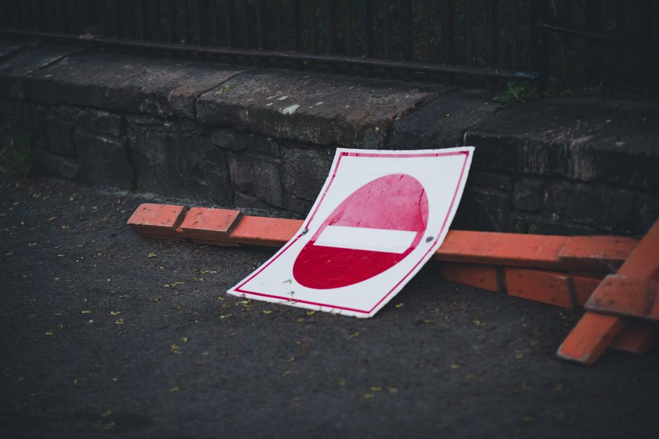 A small, light blue pickup truck parked on the side of a street with its bed fully loaded with miscellaneous rubbish, including cardboard boxes, black plastic bags, and other discarded materials. The 